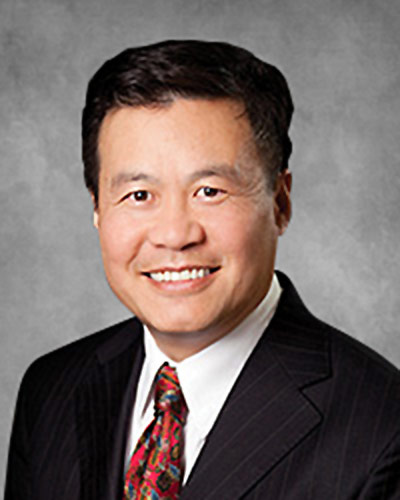 Headshot of Acuity Eye Group co-founder Tom Chang MD smiling on a grey background