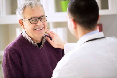 An elderly man in glasses is reassured by a doctor